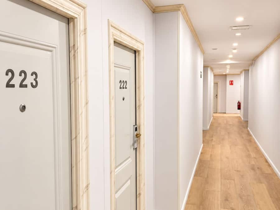 Un pasillo con puertas numeradas 223 y 222, piso de madera y luces empotradas en el techo.