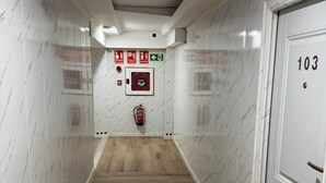 Un pasillo con paredes de mármol blanco, suelo de madera y una puerta con la inscripción '103'.