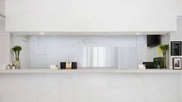 Zona de recepción de un hotel con un mostrador blanco, un televisor de pantalla plana montado en la pared y un cartel con información del hotel.