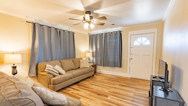 Una sala de estar con sofá, mueble para televisión y ventilador de techo.