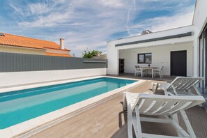 A modern outdoor pool area with a clear blue pool, white lounge chairs, and a covered patio with a table and chairs. - Villa with a pool, near Serra da Arrábida and the beaches, Azeitão, Portugal (São Simão)