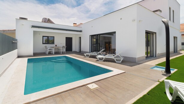Una casa moderna con piscina, mobiliario exterior y un césped cuidado.