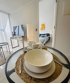 A dining table with a bowl, a wine glass, and a candle. There is a TV in the background and a bed with a yellow blanket.