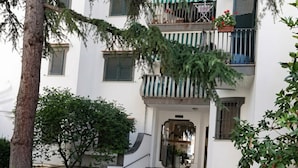 Un bâtiment avec un escalier menant à une porte, entouré de verdure et bordé d’un pavé en pierre à motifs.