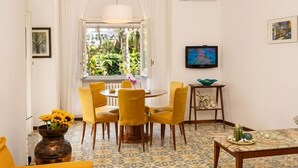 Une pièce comprenant un coin repas, un canapé, un téléviseur et une fenêtre donnant sur un paysage verdoyant.