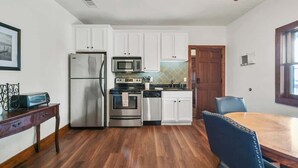 Une cuisine moderne avec des meubles blancs, des appareils en acier inoxydable et un coin repas comprenant une table en bois et des chaises bleues.