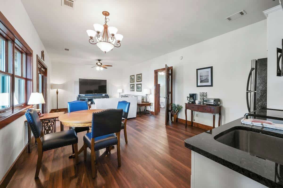 Une cuisine spacieuse dotée d’un grand îlot central, un coin repas avec une table ronde et des chaises, et un salon avec un téléviseur et des fauteuils.