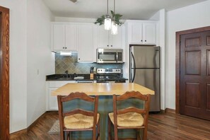 A kitchen with white cabinets, a stainless steel refrigerator, a microwave, and a stove. There are two wooden chairs with woven seats. - Lakeside Villa Retreat- 4BR/4BA in Cuscowilla (Eatonton)