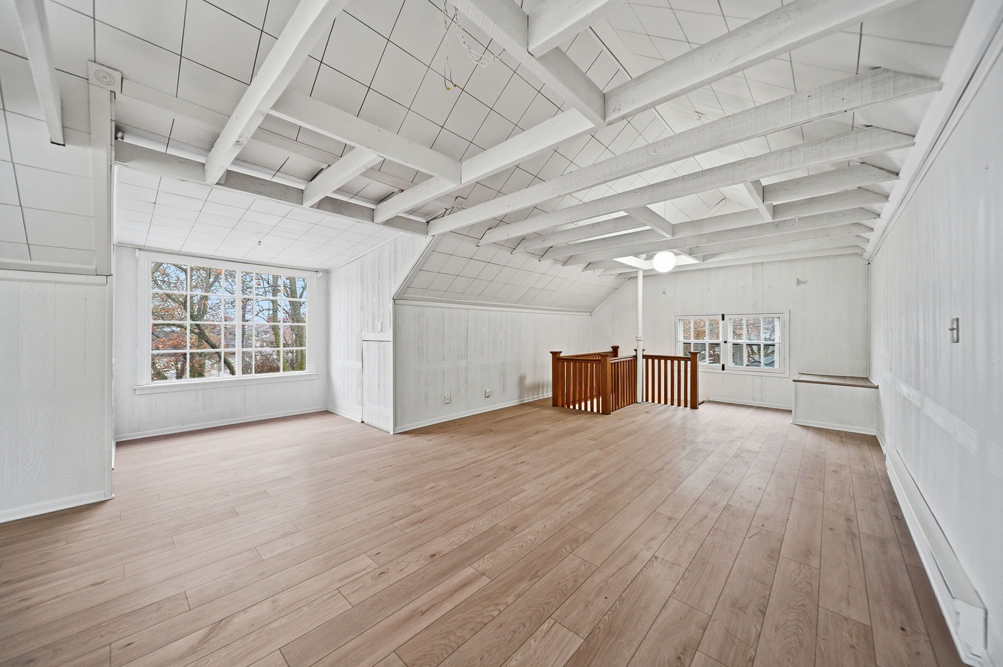 A spacious attic room with high ceilings, large windows, and wooden floors.