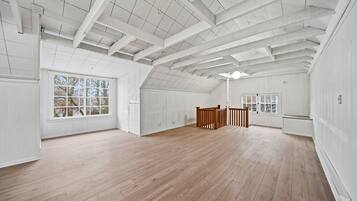 A spacious attic room with high ceilings, large windows, and wooden floors.