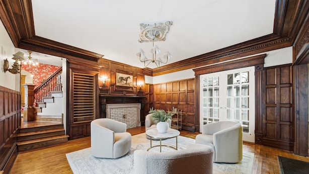 A spacious living room with a fireplace, wooden paneling, and a staircase leading to another level.