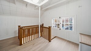 A spacious room with a wooden staircase, a large window with a view of the outside, and a high ceiling with exposed beams.
