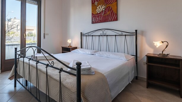 Une chambre à coucher avec un lit, deux tables de chevet, une fenêtre et un tableau au mur.
