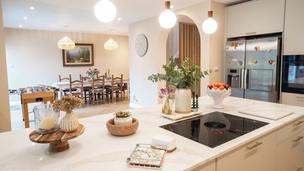 Een moderne keuken met een centraal eiland, ingebouwde apparatuur en een eethoek op de achtergrond.