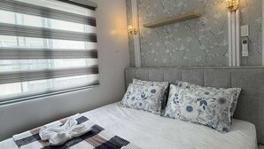 Une chambre d’hôtel avec un grand lit, une fenêtre avec des stores, un climatiseur fixé au mur et deux appliques murales.