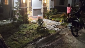 Vue nocturne d'une maison avec un jardin aménagé, une moto et une personne debout près de l'entrée.