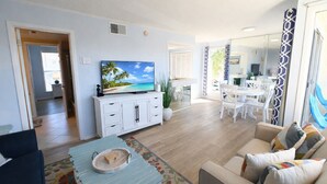 Ein Wohnzimmer mit Fernseher, weißen Möbeln, einem Essbereich und einer Küche.