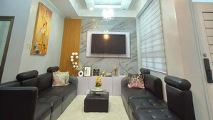 Ein modernes Wohnzimmer mit einem Flachbildfernseher, schwarzen Ledersofas, einem weißen Teppich und einer dekorativen Kronleuchter.