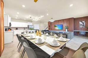 Een moderne keuken met witte kastjes, een centraal eiland en een eetgedeelte voor zes personen, met een lange tafel en zes stoelen.