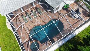 Vista aérea de una piscina con bordeado de azulejos, rodeada de sillones de descanso y una zona de estar cubierta.