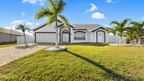 A modern two-story house with a garage, a well-maintained lawn, and palm trees.