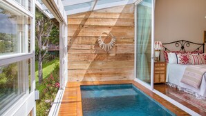 A bedroom with a large window, a wooden wall, a small pool, and a bed with pillows.