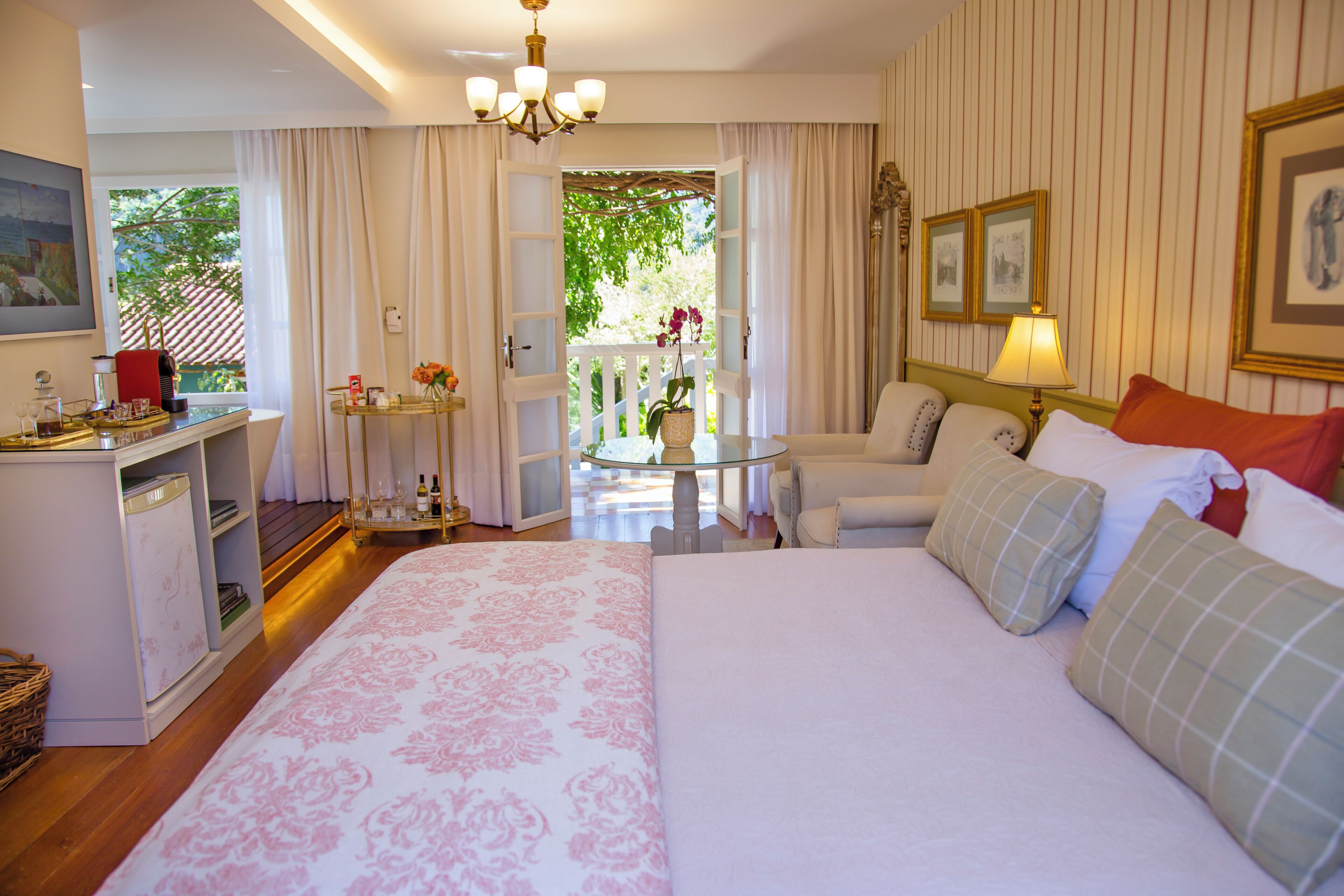 Une chambre d’hôtel comprenant un lit, un bureau, une chaise, une table avec un pot de plante et un balcon donnant sur un paysage verdoyant.