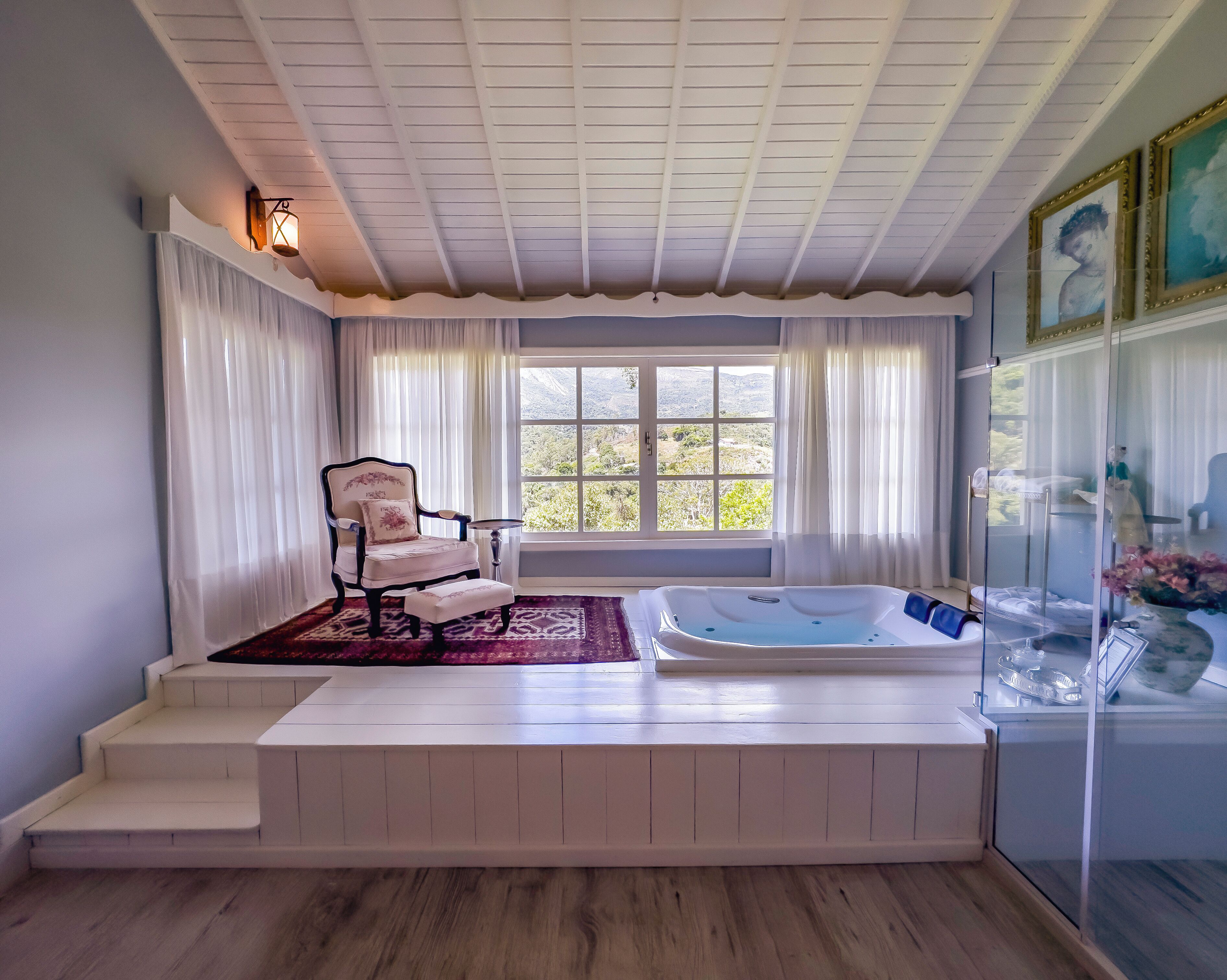 Un cuarto de spa con una bañera, una silla y un ventanal con cortinas.