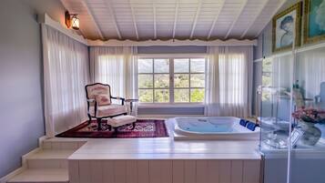 Un cuarto de spa con una bañera, una silla y un ventanal con cortinas.