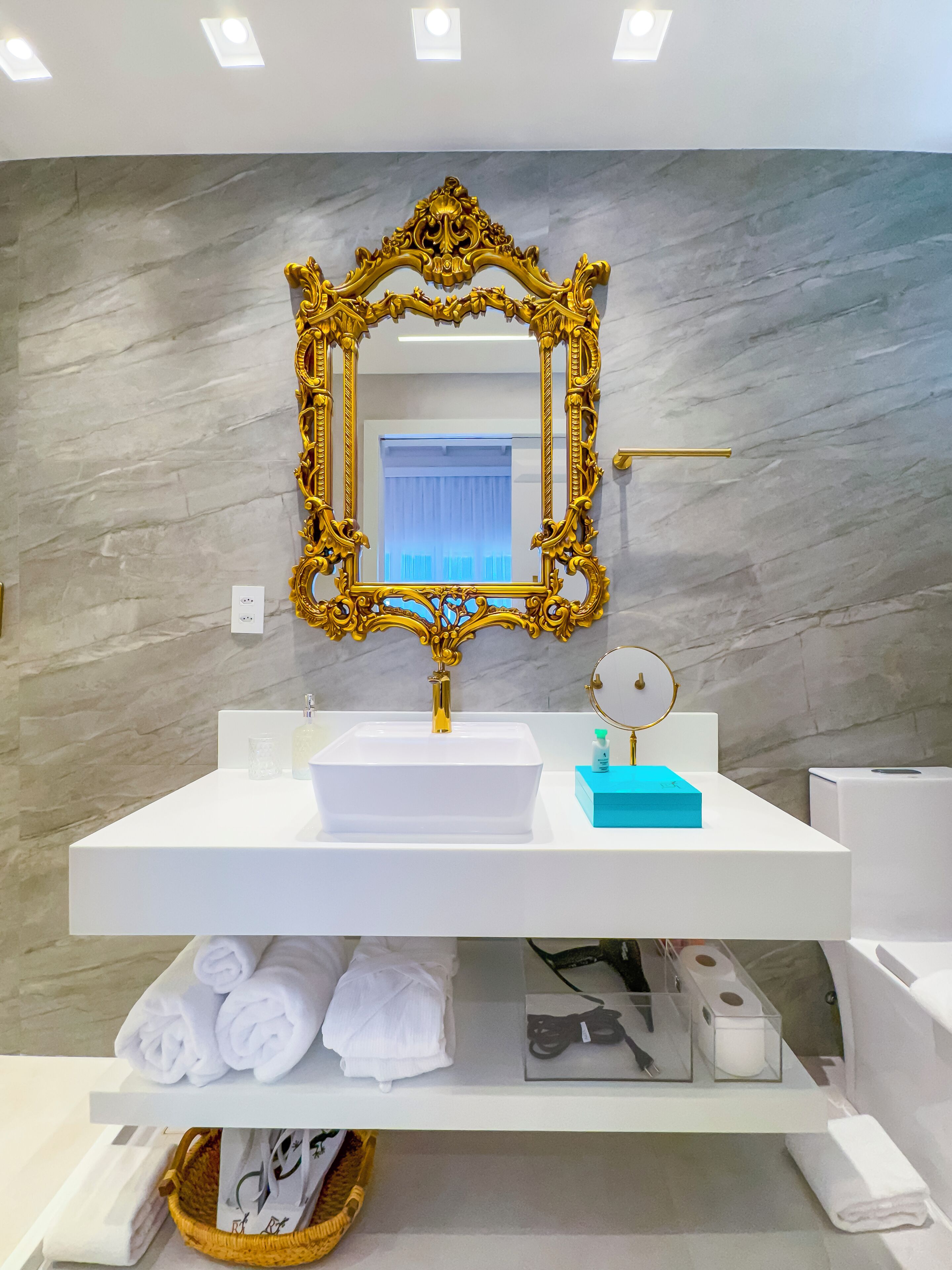 Une salle de bain avec un lavabo blanc, un miroir doré à motifs et des murs en marbre.