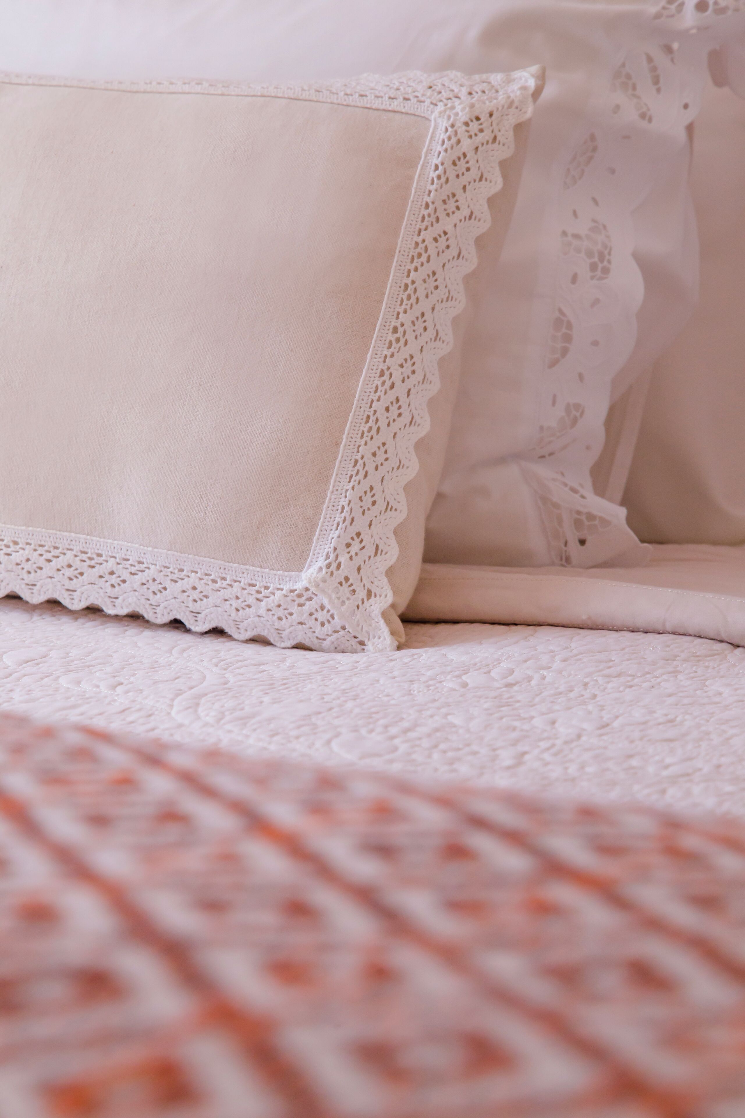 A bed with a white pillow and a white pillowcase with lace trim.