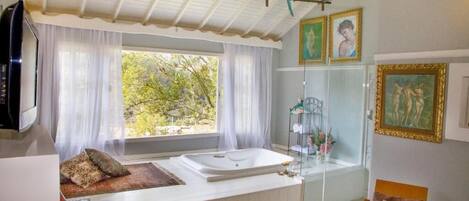Una habitación con una bañera grande, un televisor y un ventanal con cortinas.