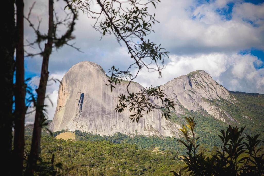 Une vaste formation rocheuse naturelle, avec une cascade, entourée d’une forêt dense et de montagnes.