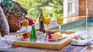 A table set with a cheese platter, fruits, wine glasses, and bottles by a poolside.