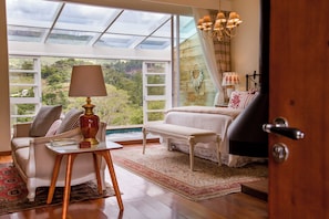 Una habitación con un ventanal grande, un sofá, una silla, una mesa con lámpara y una cama.