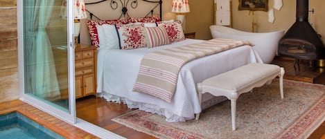 A bedroom with a glass door leading to a pool, a bed with white bedding, a chandelier, and a fireplace.