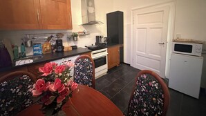 Une cuisine compacte avec des meubles en bois, une cuisinière, un four à micro-ondes et un coin repas agrémenté d’une nappe à motifs floraux.