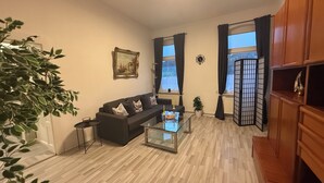 Un salon avec un canapé, une table basse en verre, une plante et un tableau accroché au mur.