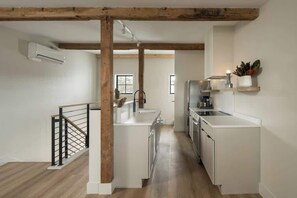 A modern kitchen with white cabinetry, a wooden ceiling beam, and a black railing. - Eagle at the Mill - 2 (Westport)