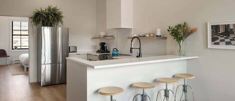 A modern kitchen with a central island, bar stools, a stainless steel refrigerator, and a potted plant.