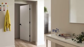 A modern, minimalist room with a wooden floor, a white wall-mounted air conditioner, a door leading to another room, and a desk with a potted plant and books. - Owl at the Mill  - 3 (Westport)