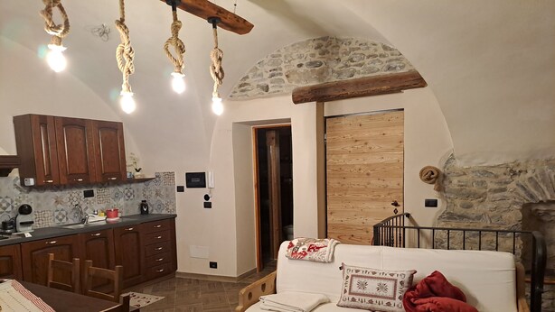 Ett mysigt rum med en soffa i trä, ett matbord och en köksdel med träskåp och en vägg av sten.