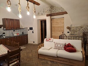 Een gezellige kamer met een houten bank, een eettafel en een keukenhoek met houten kastjes en een stenen muur.