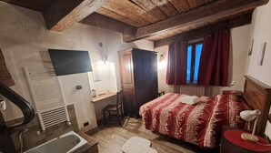 Ett mysigt sovrum med ett träpanelat tak, en säng med ett mönstrat överkast, ett skrivbord med en stol, ett element och ett fönster med röda gardiner.