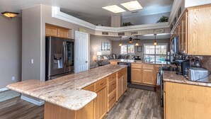 A spacious kitchen with granite countertops, wooden cabinets, a built-in refrigerator, and a large island. - Havasu Tropics - Pool, Spa, Game Room, Sleeps14 (Lake Havasu City)
