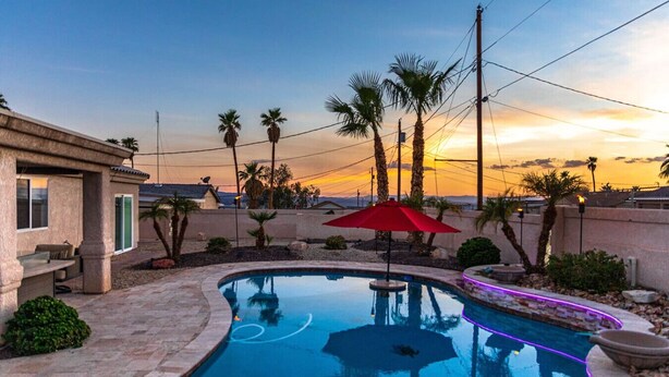 A swimming pool with a red umbrella, palm trees, and a sunset view. - Havasu Tropics - Pool, Spa, Game Room, Sleeps14 (Lake Havasu City)