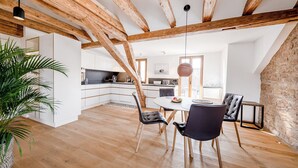Une cuisine moderne avec des meubles blancs, un plafond en bois et un coin repas comprenant une table ronde et des chaises.