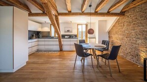 Un loft spacieux avec des poutres apparentes, une cuisine dotée de meubles blancs et un coin repas avec une table ronde et des chaises.
