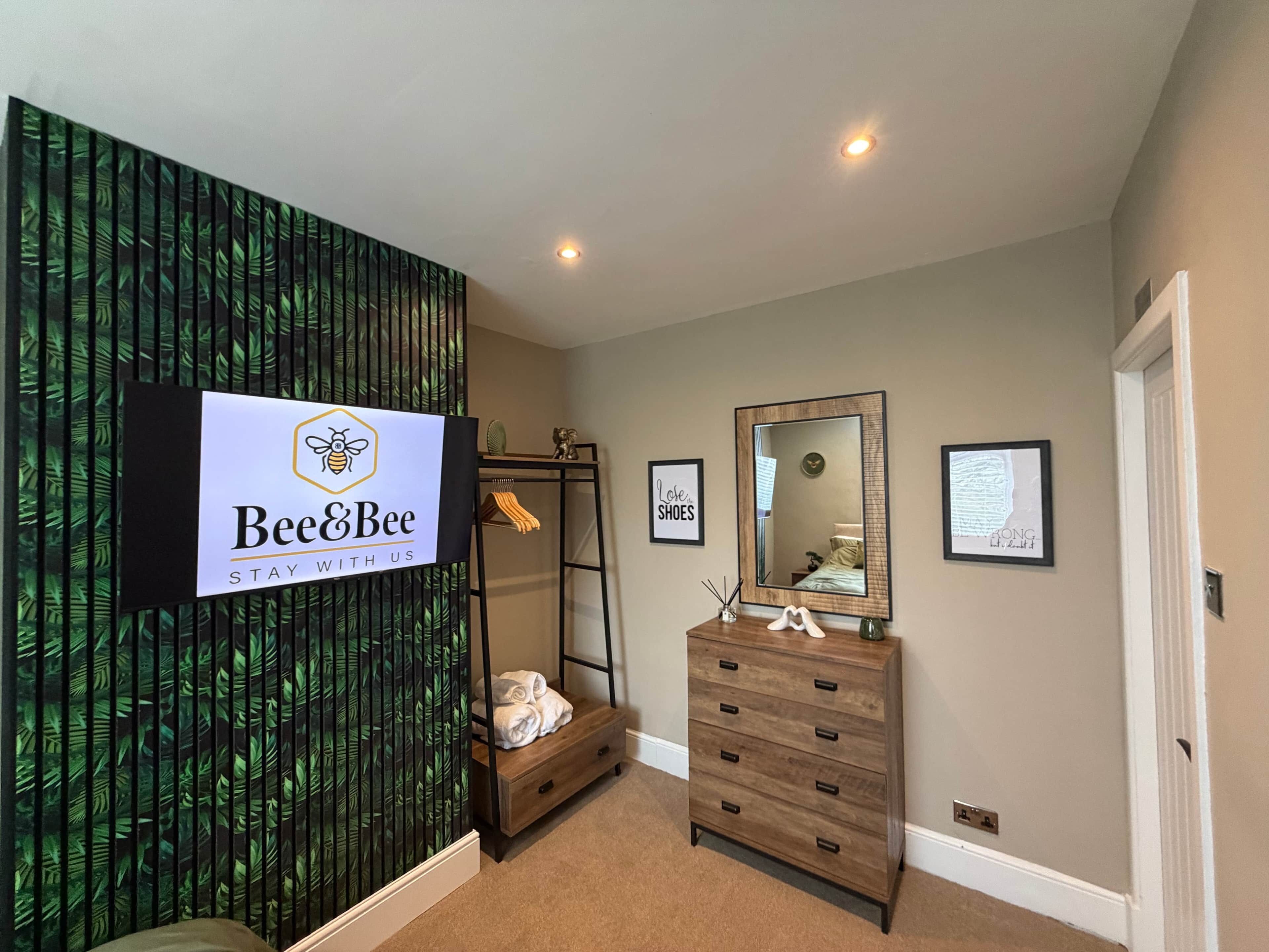 A hotel room with a large mirror, a wooden dresser, a wall-mounted sign, and a shelf with towels.