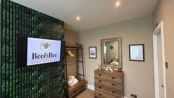 A hotel room with a large mirror, a wooden dresser, a wall-mounted sign, and a shelf with towels.